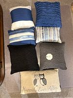 Photo showing seven decorative pillows in various styles, colors, and textures arranged on the floor.
