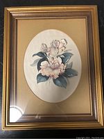 Front view of gold framed floral picture showing an oval white background with a flower painting, set on beige mat.