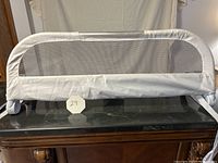 White kids bed rail with a protective mesh bar, positioned upright on a wooden table.