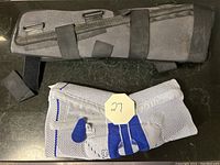 Photo of dark gray knee brace with velcro straps above light gray and blue knee support brace on black surface.