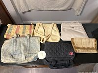 Photo of six assorted purses and bags arranged on a table showing sizes, colors and material types.