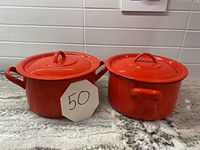Photo of two red metal pots with lids on a countertop, showing exterior and handles