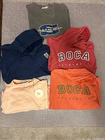 Photo showing five hoodies and pullovers: Grey Guess, Dark Blue Wind River, Red BOCA Football, Peach/Pink Pullover, Orange BOCA Authentic.