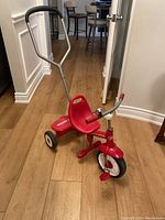 Full view of red Radio Flyer tricycle showing seat, pedals, front wheel, and push handle with black foam grip.