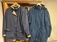 Navy blue jackets with buttons and beige lining shown hanging on wooden hangers