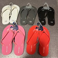 Five pairs of Old Navy women's flip flops in size 9-10, assorted colors on a textured surface, displayed with hangers attached.