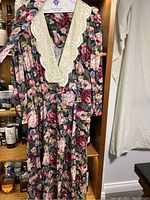 Photo of a women's long floral dress with cream lace V-neck collar and matching belt hung on a hanger.