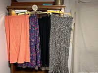 Seven skirts hanging on a rack showing front views. From left to right: peach solid skirt with buttons, dark floral skirt, solid black skirt, black and white animal print skirt.