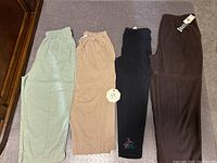 Four pairs of pants in mint green, beige, black with floral detail, and dark brown with tags.