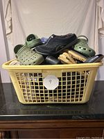 Full view of woven basket containing assorted used women's shoes including Crocs, Skechers, dress shoes, and sandals stacked inside.