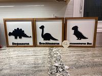 Front view of the three wood framed dinosaur silhouette pictures arranged side by side on a countertop.
