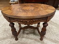 Oval wood side table showing inlaid top and carved details on apron and legs.