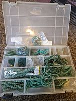 Top-down view of plastic compartment container holding various strands and bags of green aventurine beads and carved bead pieces.