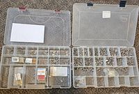 Two plastic containers filled with assorted small jewelry findings such as charms and jump rings sorted in compartments.