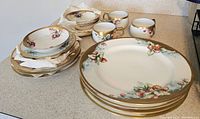Full view of the set with stacked plates and cups featuring varied floral motifs and gold rims.