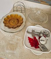 Overview of kitchen serving items arranged on counter including amber glass plates, clear bowl, ceramic tray with cookie cutters, and metal napkin holder