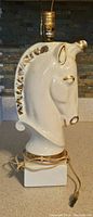 Side view of white ceramic horse head lamp showing gold accents and wiring wrapped on base.