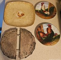Four items arranged in a square: two rooster-themed ceramic plates, one rectangular platter with a rooster in the center, and a round divided cast iron trivet with patina.