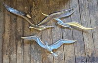 Three vintage metallic finish bird wall art pieces placed on wooden floor, showing all three birds together.