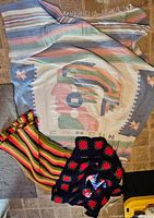 Full view of three blankets layered together showing the Cancun souvenir woven blanket and the colorful crocheted and striped blankets.