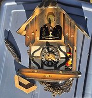 Overview of vintage wooden cuckoo clock with detached parts including pinecone weight and wood base piece, showing rustic painted floral accents and front view.