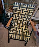 Full view of one folding chair showing patterned fabric seat and back, wooden armrests, and green metal frame.