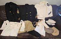 Overview of the collection showing two dark navy naval jackets, white uniform shirts, and multiple hats arranged on a couch.