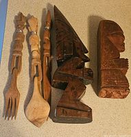 Top-down view of wooden fork, spoon, and two carved figurines showing design details and wood tones.