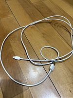 White charging cables for iPhone and Android devices laid on wooden floor, showing USB and lightning connectors.