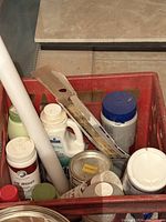 Red plastic crate containing assorted hot tub cleaning chemicals and accessories, various bottles and a white PVC pipe visible.