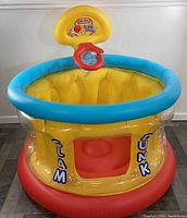 Front view of fully inflated ball pit with the basketball hoop and branded 'Slam Dunk' logo visible. Yellow body with blue rim and red base.