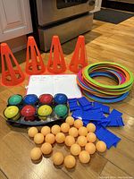 Orange plastic cones, colorful rings, small foam balls, orange ping pong balls, blue scoring clips on hardwood floor