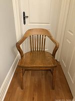 Front right angle of a solid wood chair showing curved armrest, slatted backrest, and seat surface with visible wood grain.