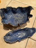 Two blue pottery bowls shown from above on tiled surface, highlighting shape and texture resembling leaves with vein details.