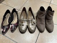 Three pairs of women's shoes: black floral Christian Siriano flats, gold Nine West Oxford loafers, and brown Fergalicious suede booties.