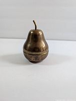 Photo of the brass pear-shaped container standing upright showing its detailed pear form and stem.