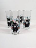 Front and slightly angled view of four tall clear glass drinking cups arranged in a cluster, each with black cat and floral window design