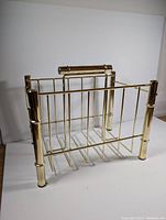 Front and side view showing the open-frame design, cylindrical legs, and horizontal bar handle in gold tone metal.
