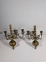 Front view of the pair of vintage brass wall sconces showing three candle holders each with decorative curved arms and aged brass finish.