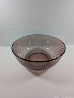 Oblique side view of cranberry colored ribbed glass mixing bowl showing translucent textured pattern and flared rim.