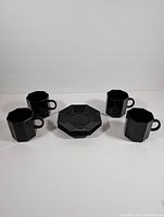 Set of four black glass octagonal tea cups arranged around four matching octagonal saucers on a white surface with plain background.