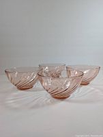 Four vintage pink swirl Arcoroc glass bowls arranged spaced apart showing embossed swirl pattern in translucent pink glass.