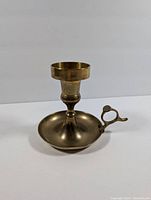 Side perspective of vintage brass candle holder showing round base, stem, and cup-shaped candle holder with finger loop handle.