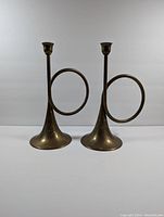 Pair of vintage brass horn-shaped candlestick holders shown from front, displaying their unique horn loop design and aged patina.