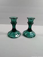 Pair of emerald green glass candlestick holders shown from front angle on white background.