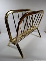Angle view of the vintage gold tone metal magazine and vinyl record rack showing vertical bars and angled legs.