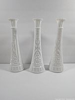 Front-facing image showing set of three tall vintage milk glass vases with textured geometric patterns and scalloped rims.