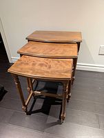 Three vintage wooden nesting side tables stacked nested together showing wood tops and turned legs.