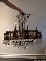 Overall view of chandelier held by its top hook showing metal filigree frame and hanging crystal strands