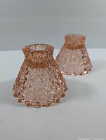 Two pink cubic depression glass candlestick holders shown at an angle to highlight texture and shape.